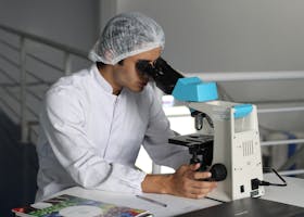 Scientist in a lab coat using a microscope to conduct research, focusing on healthcare improvements.